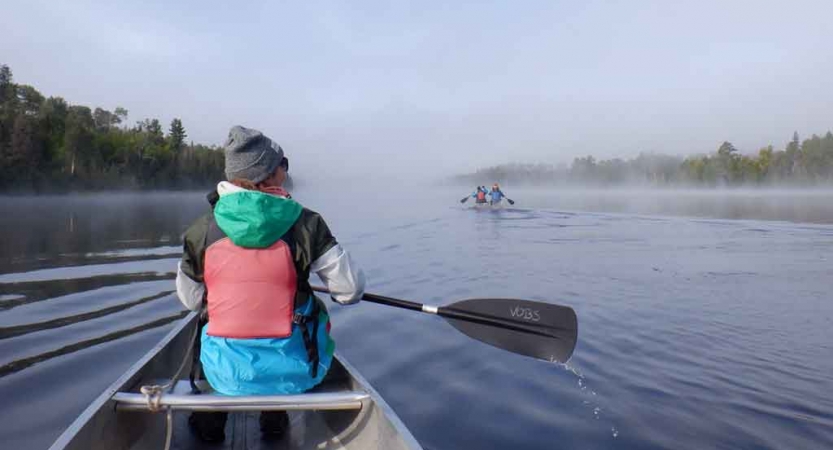 a student in a canoe paddles on calm water into the fog 